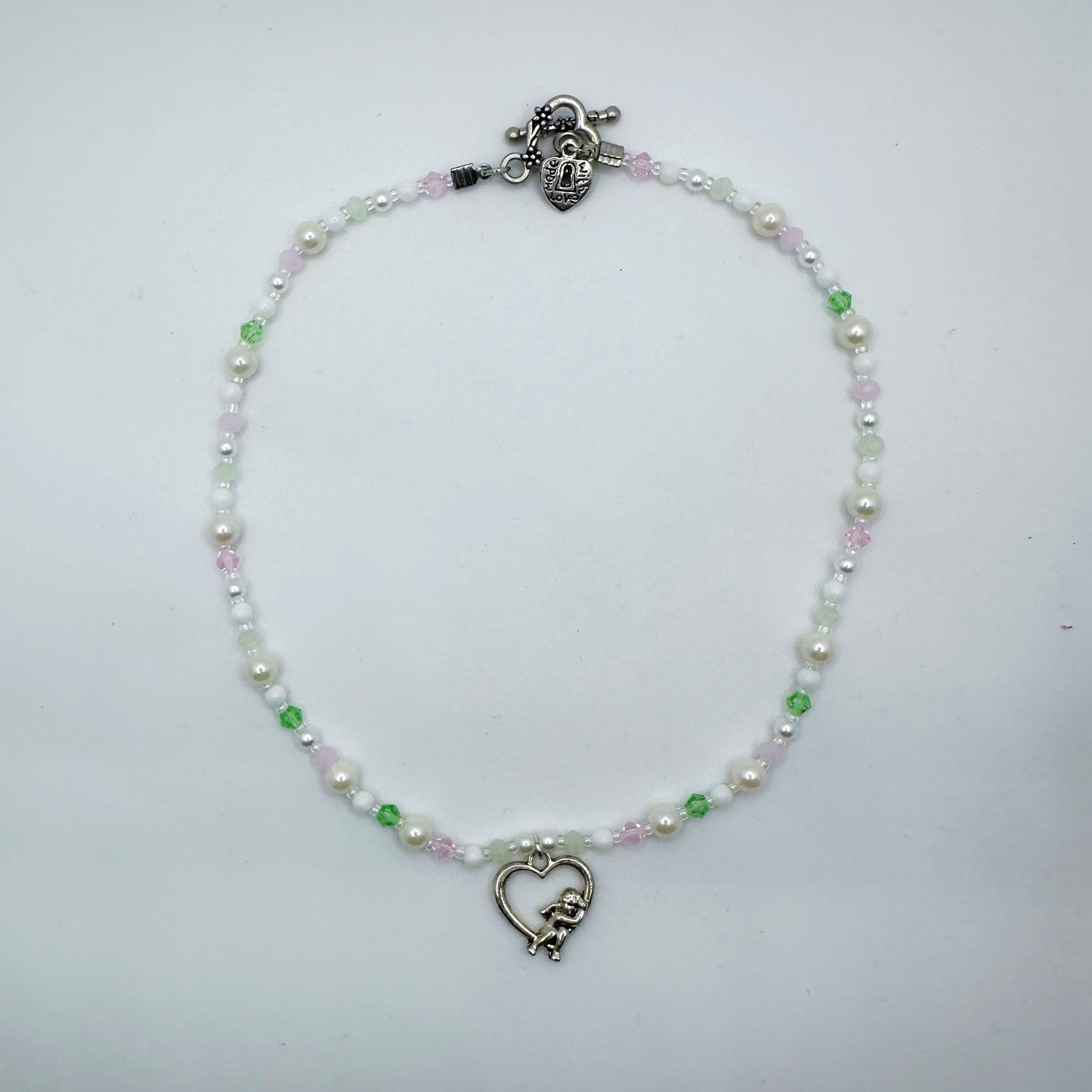 Pastel beaded necklace with faux pearls, green and pink glass beads, and a silver heart cupid charm – handmade girly fairycore jewellery by Daisy Chikk