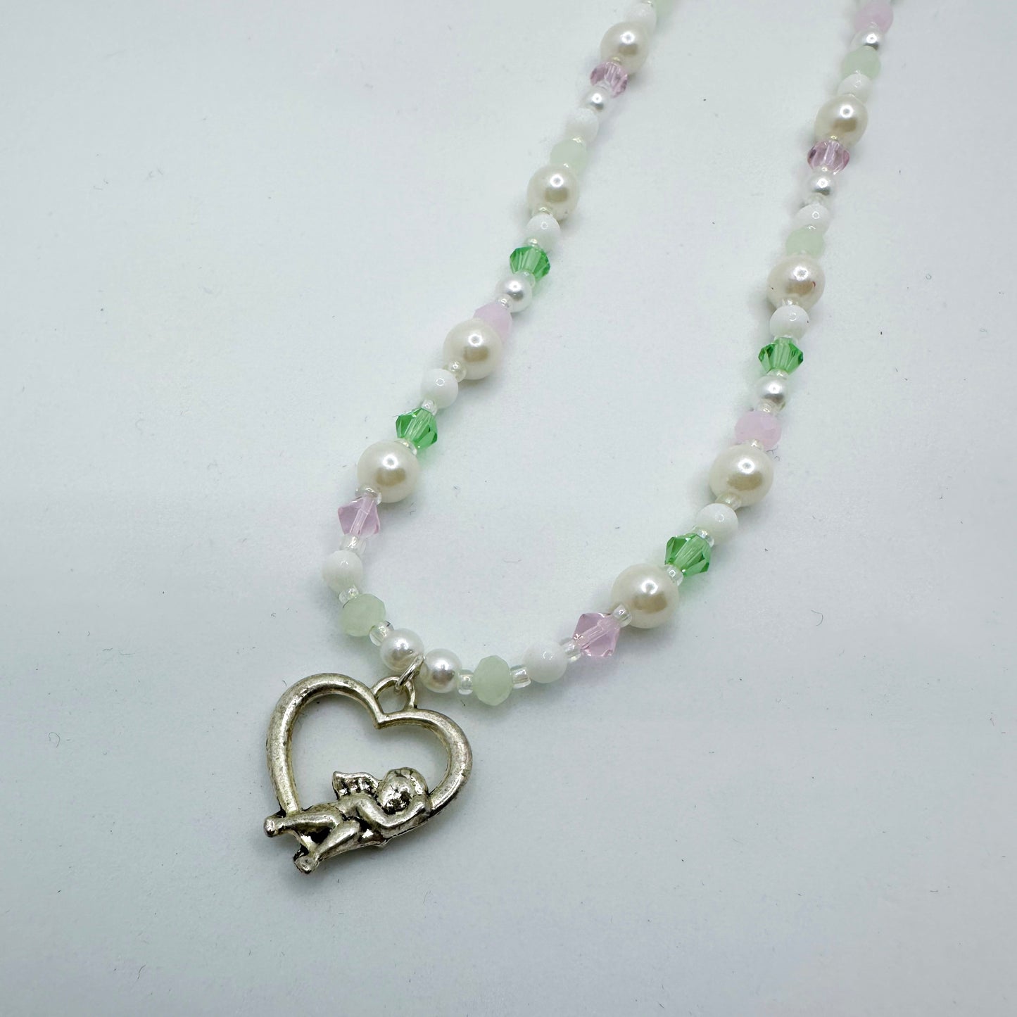 Close-up of a pastel beaded necklace with white pearls, pink and green crystals, and a silver cupid in heart charm – handmade fairycore Y2K jewellery