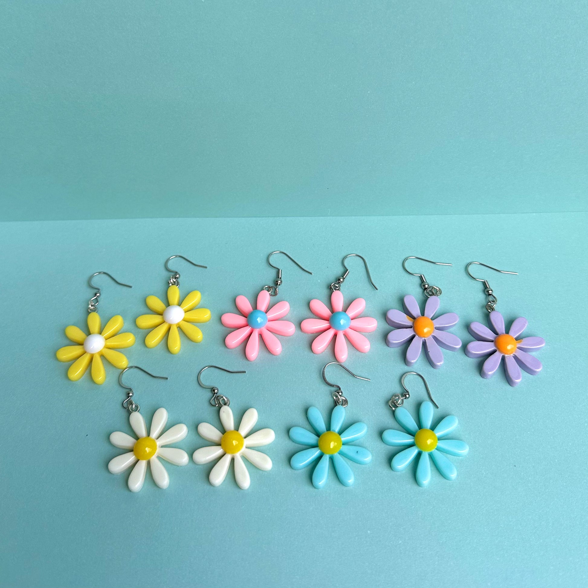 Assorted daisy earrings in pastel colours including yellow, pink, blue, purple and white with silver hooks – handmade Y2K floral statement jewellery by Daisy Chikk