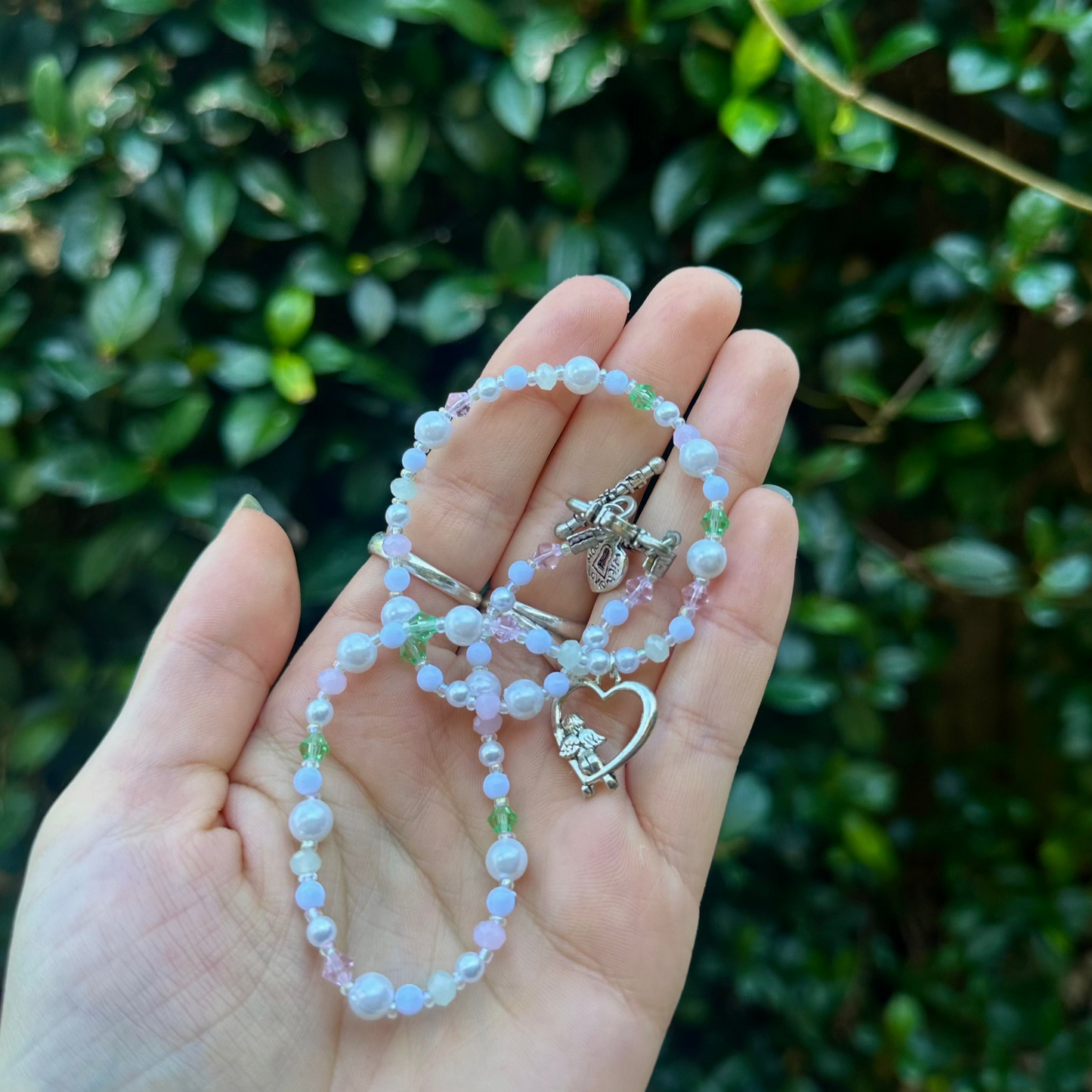 Side view of a pastel beaded necklace with pearls, pink and green crystals, and a silver heart charm with a cupid figure – romantic handmade fairycore jewellery