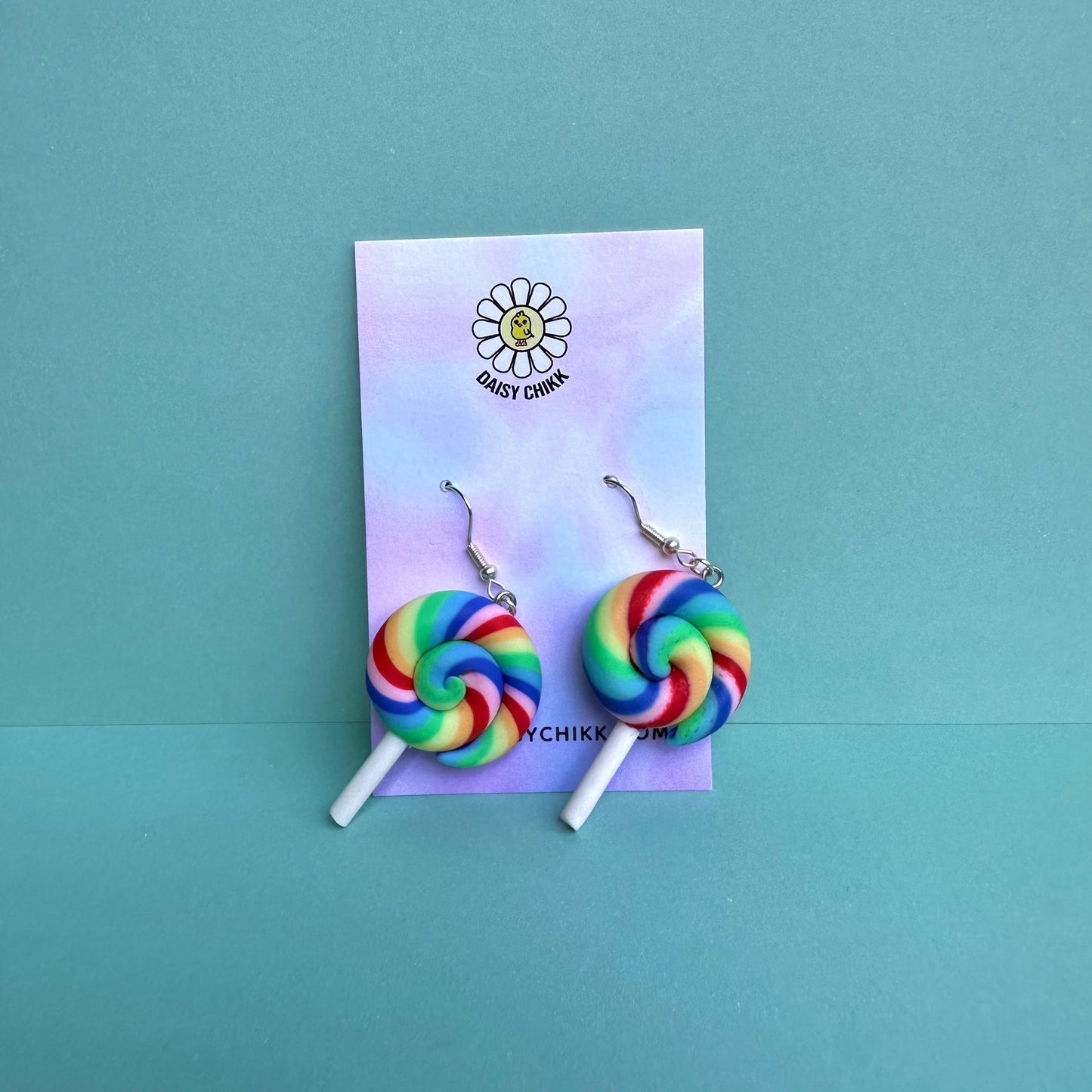 Rainbow swirl lollipop earrings with white sticks and silver hooks displayed on a pastel Daisy Chikk backing card – handmade kawaii dopamine-core jewellery