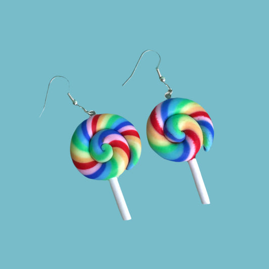 Rainbow swirl lollipop earrings with white sticks and silver hooks on a blue background – handmade kawaii dopamine-core jewellery