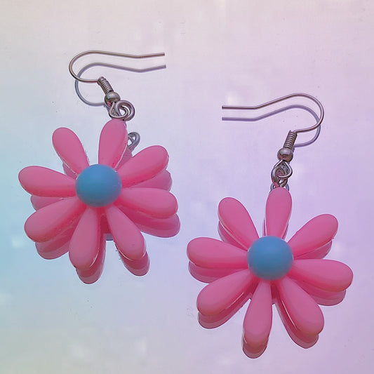 Close-up of pink daisy earrings with white centre and silver hooks on iridescent rainbow background – pastel soft girl Y2K jewellery aesthetic