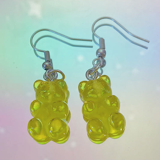 Close-up of translucent yellow gummy bear earrings with silver hooks on a dreamy pastel rainbow background – kawaii Y2K handmade jewellery