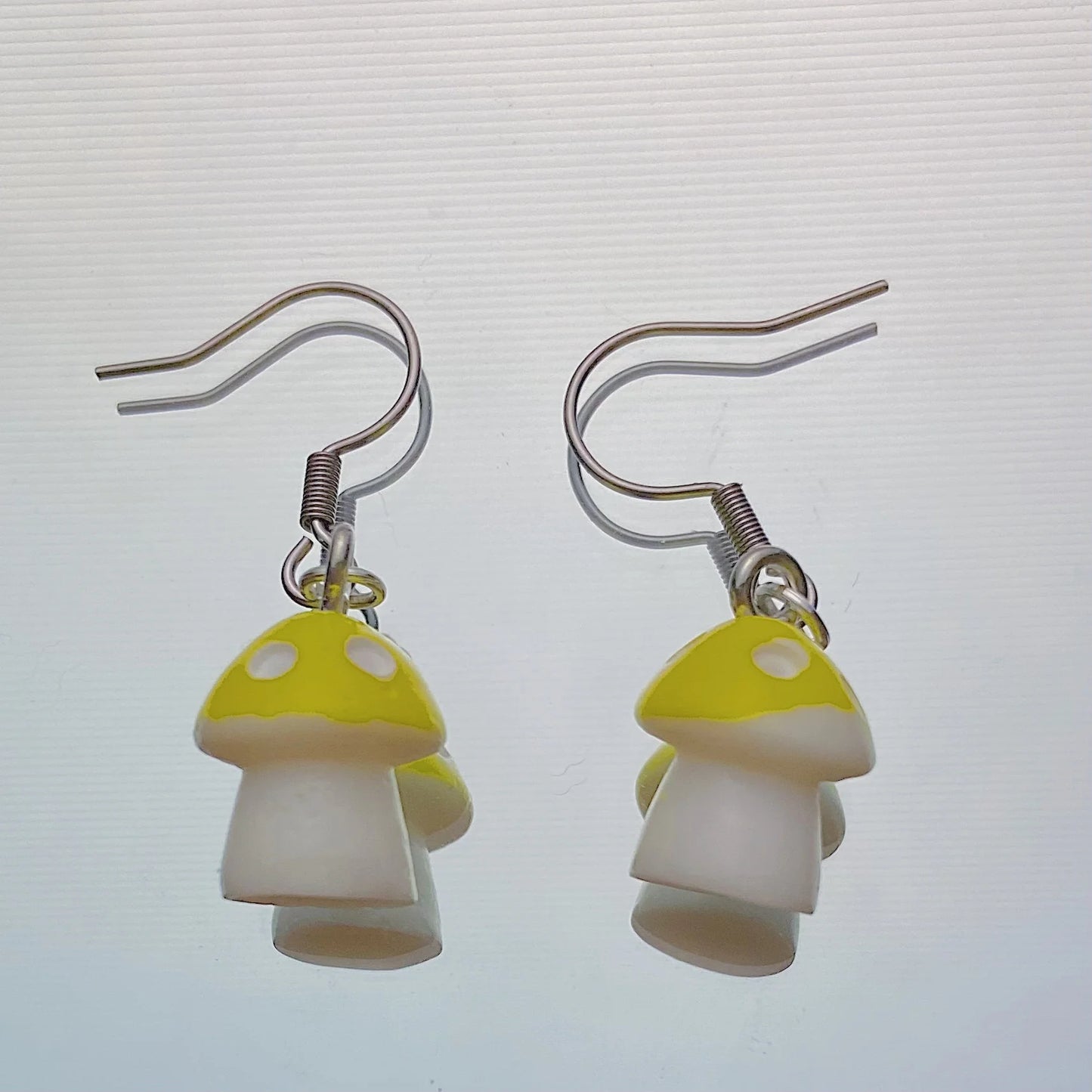 Yellow mushroom earrings with white stems and silver hooks shown on a white background – handmade kawaii resin dangle jewellery, 35 x 13 mm
