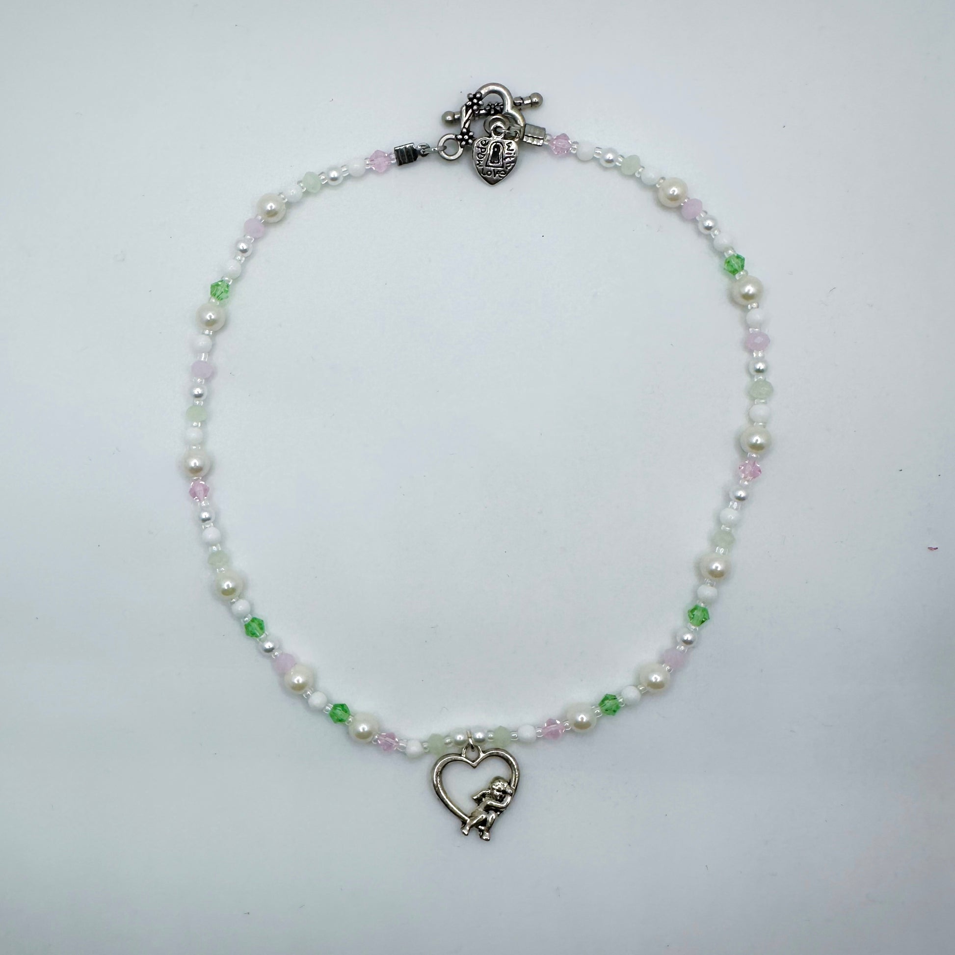 Pastel beaded necklace with faux pearls, green and pink glass beads, and a silver heart cupid charm – handmade girly fairycore jewellery by Daisy Chikk