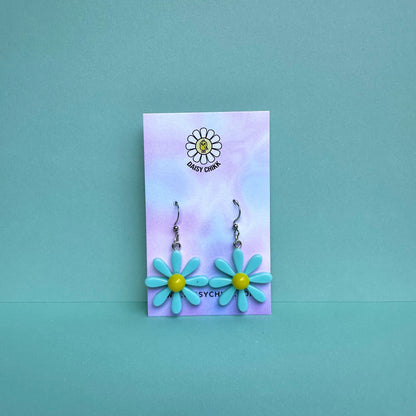 Blue daisy flower earrings with white centre on silver hooks, displayed on pastel Daisy Chikk backing card – kawaii handmade statement jewellery
