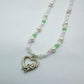 Close-up of a pastel beaded necklace with white pearls, pink and green crystals, and a silver cupid in heart charm – handmade fairycore Y2K jewellery