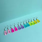 Full set of colourful gummy bear earrings in pink, purple, blue, green, and yellow arranged in a row on pastel aqua background – kawaii handmade resin jewellery by Daisy Chikk