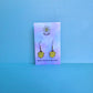 Pompompurin earrings on Daisy Chikk pastel earring card with purple and blue ombré background – handmade Sanrio-style kawaii jewellery