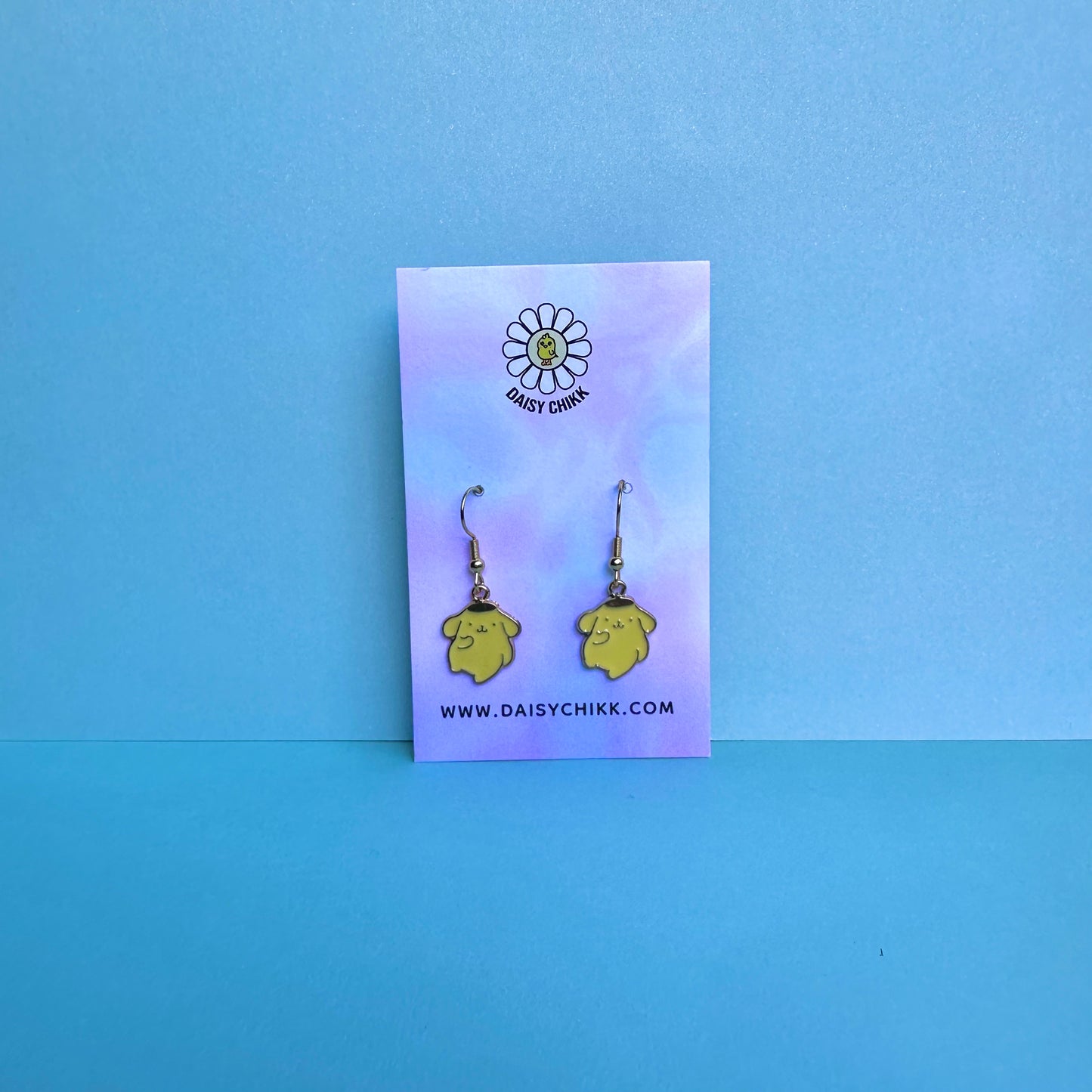 Pompompurin earrings on Daisy Chikk pastel earring card with purple and blue ombré background – handmade Sanrio-style kawaii jewellery