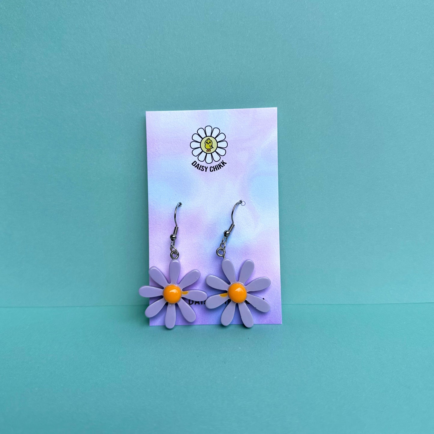 purple daisy flower earrings with white centre on silver hooks, displayed on pastel Daisy Chikk backing card – kawaii handmade statement jewellery