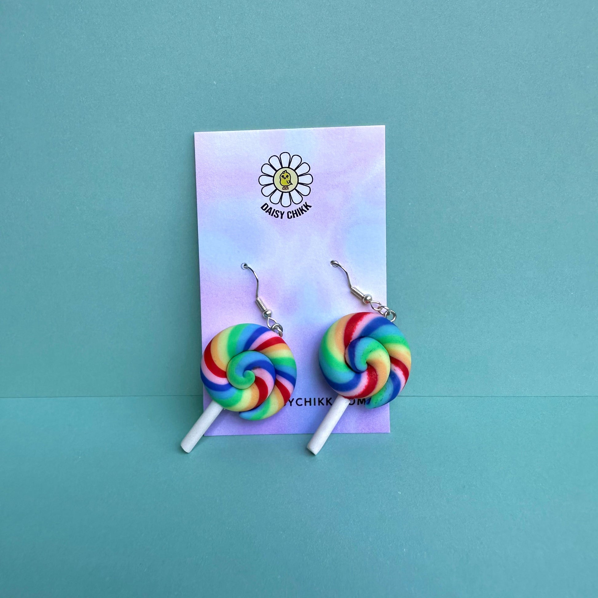 Rainbow swirl lollipop earrings with white sticks and silver hooks displayed on a pastel Daisy Chikk backing card – handmade kawaii dopamine-core jewellery