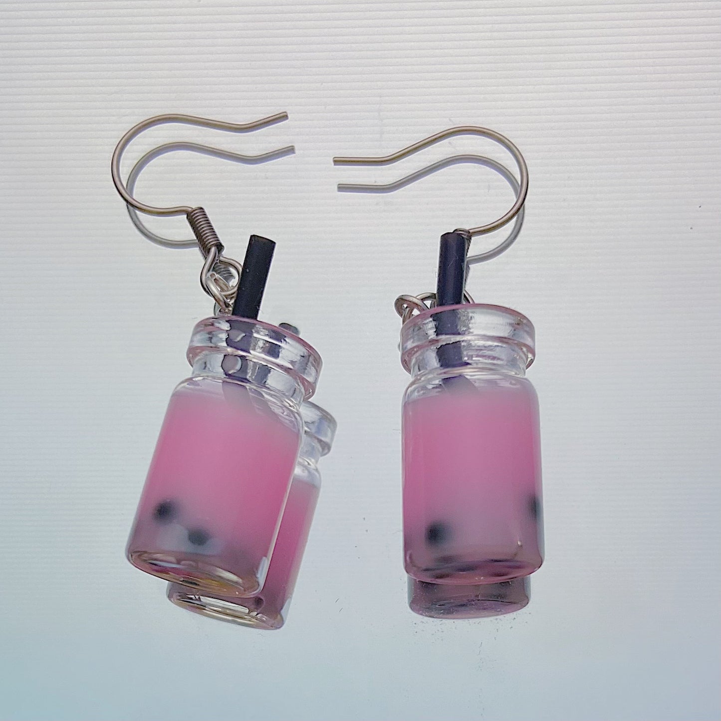 Close-up of handmade pink boba tea earrings with black straws and silver hooks – kawaii resin bubble tea jewellery