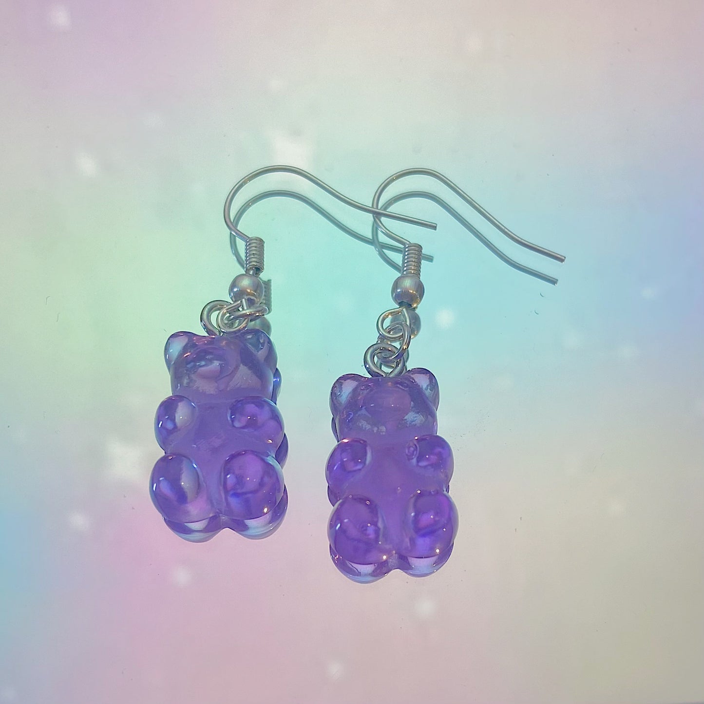 Close-up of translucent purple gummy bear earrings with silver hooks on a dreamy pastel rainbow background – kawaii Y2K handmade jewellery