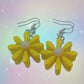 Close-up of yellow daisy earrings with white centre and silver hooks on iridescent rainbow background – pastel soft girl Y2K jewellery aesthetic